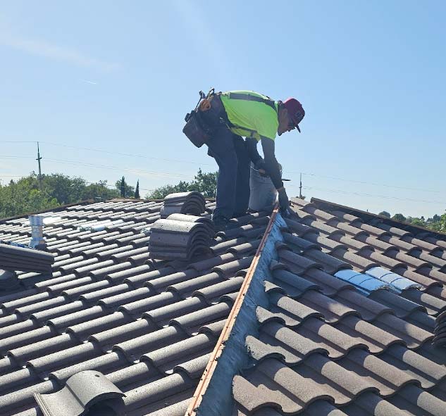 An experienced roofing technician from Bear Mountain Roofing performing a precision tile roof repair on a steep-slope residential home, focusing on sealing critical ridge lines and replacing cracked concrete tiles.